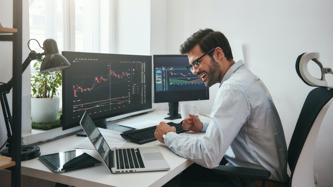 Lucky day. Happy young businessman or trader in formalwear and eyeglasses using laptop and smiling