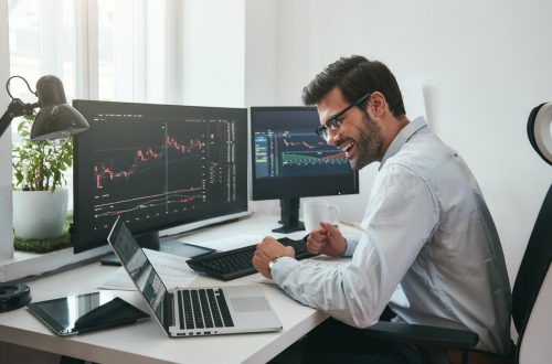 Lucky day. Happy young businessman or trader in formalwear and eyeglasses using laptop and smiling